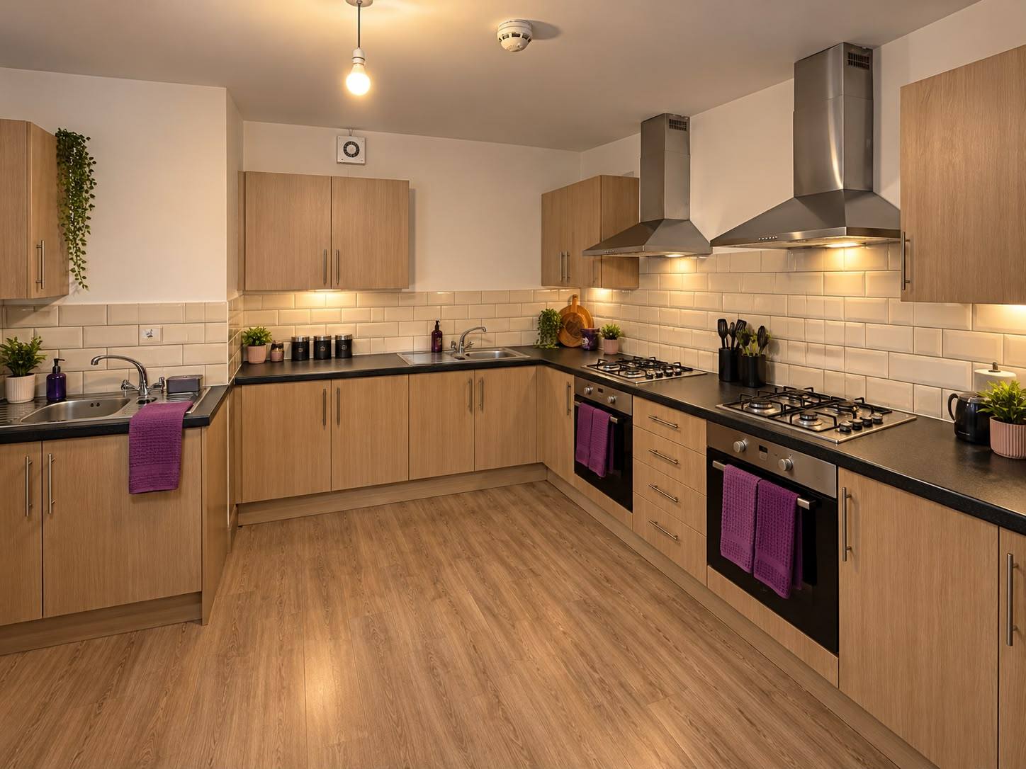 A large shared kitchen with oak cupboards, two ovens and hobs, two sinks and plenty of worktop space.