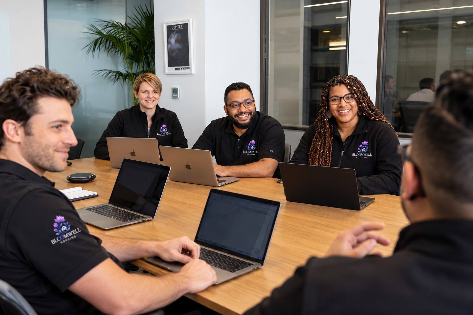 Bloomwell team members in branded tops smiling around a meeting table with laptops.